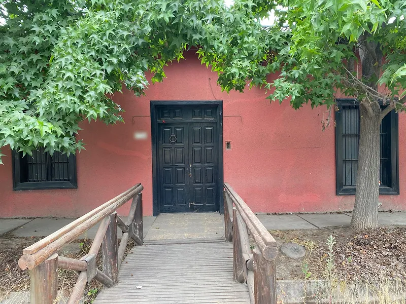 Casa antigua de muros rojos, con puerta de madera y ventanas enrejadas, en una esquina del sector Villaseca de Buin