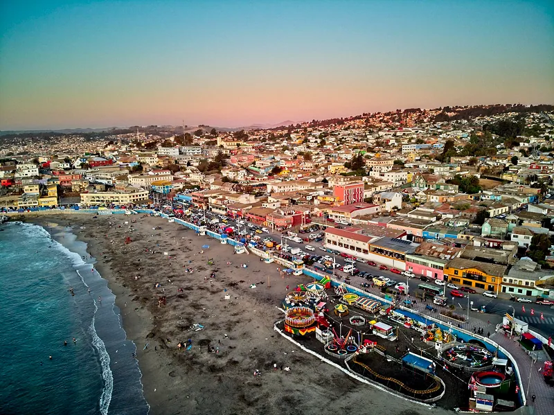 Vista aérea de Cartagena al atardecer: la playa, la costanera con juegos y el pueblo en los cerros