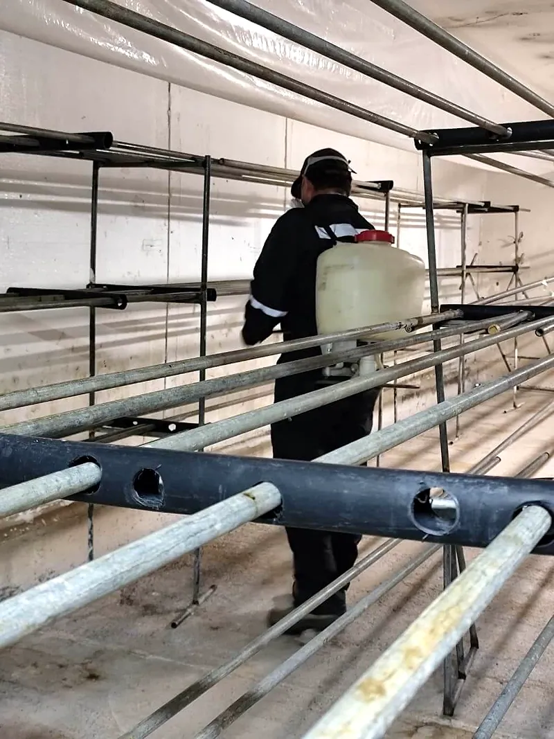 Técnico con bomba de espalda recorre los racks metálicos de una bodega durante la aplicación