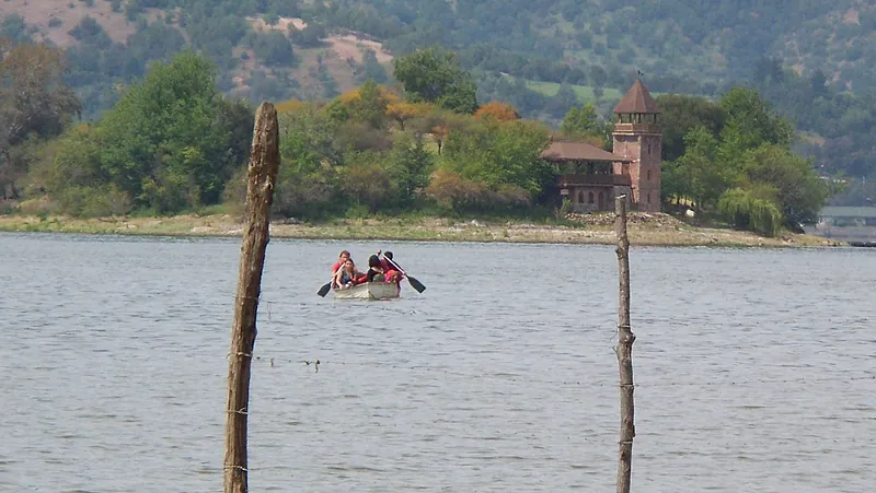 Laguna de Aculeo con agua: un bote a remo frente a una isla con árboles y una casona con torre