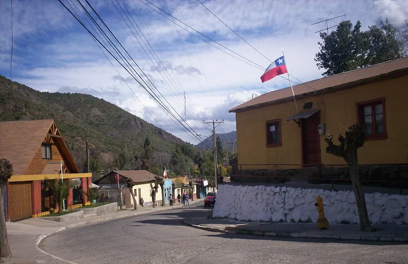 Calle del pueblo de Coya, en Machalí: casas de uno y dos pisos, una bandera chilena y los cerros de fondo