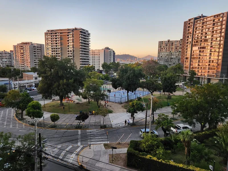 Plaza Zañartu, en Ñuñoa, con árboles y juegos, rodeada de edificios de departamentos al atardecer