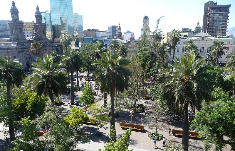 Plaza de Armas de Santiago vista desde lo alto, con palmeras, jardines, bancas y la Catedral Metropolitana a la izquierda