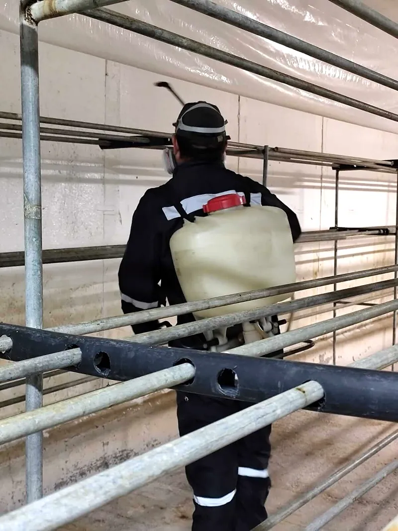 Técnico de espaldas fumiga entre los racks metálicos de una bodega con bomba de espalda